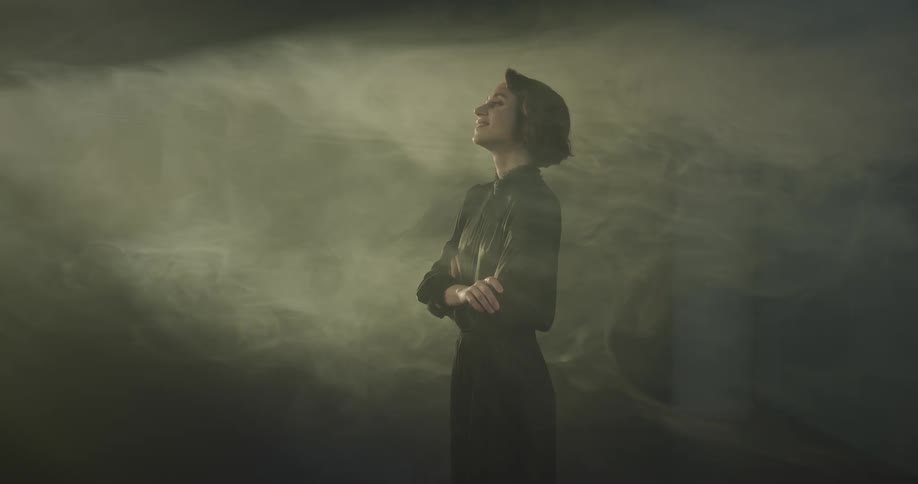 A woman stands with arms crossed and smiling as natural light illuminates her