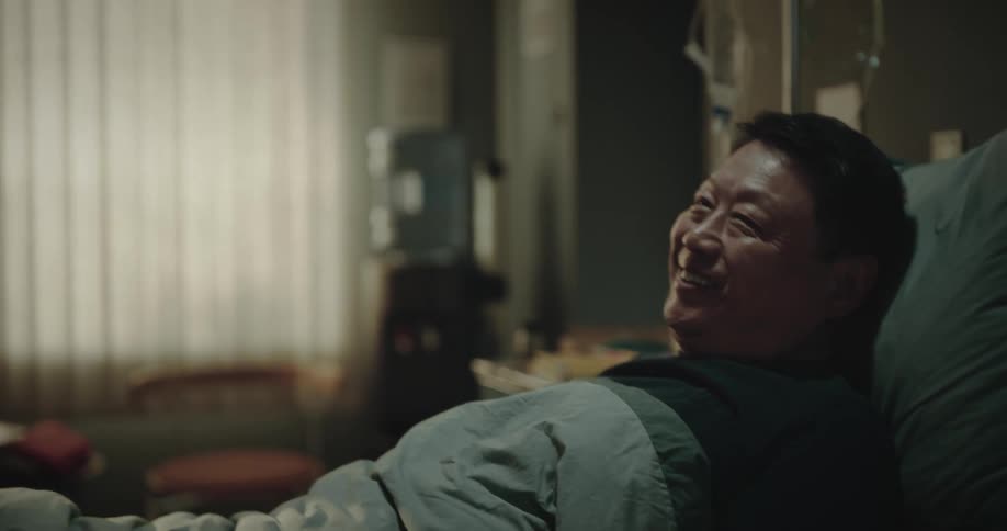 Man lying in the hospital bed reading a book he is surprised by his family bringing him a small birthday cake and balloons for a small celebration