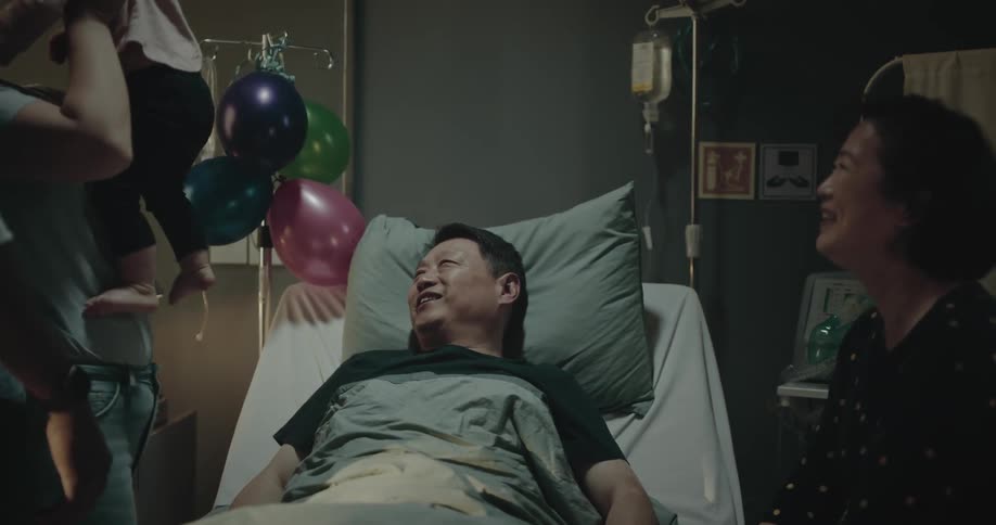A man is lying in a hospital bed and his family is around him and everyone is happy