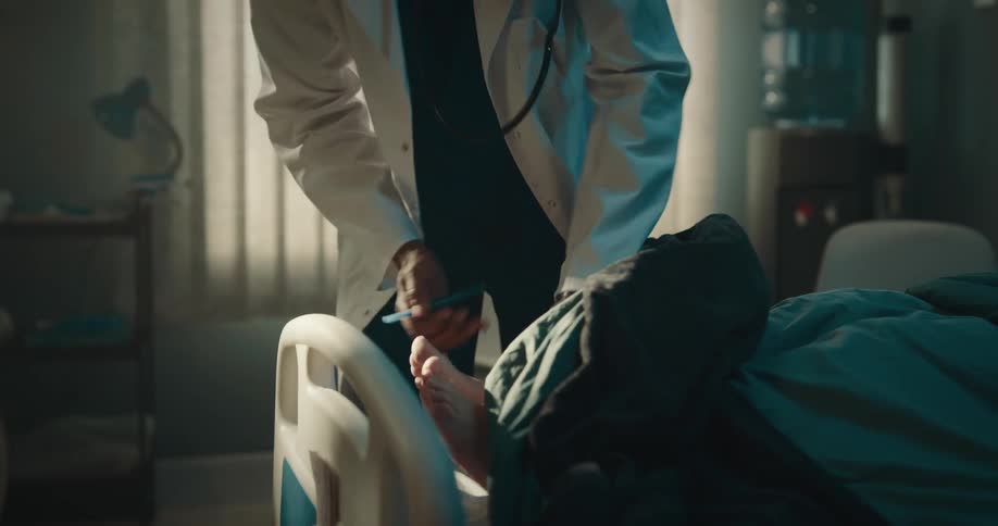 Doctor examining the feet of a patient who is sitting on the hospital bed