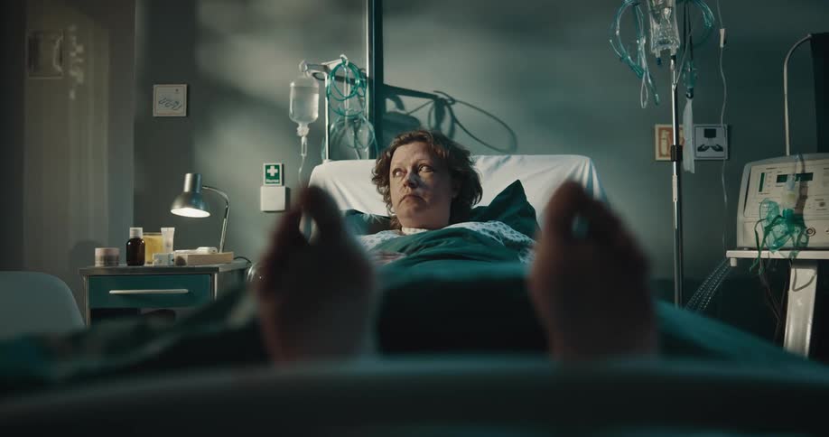 A woman in a hospital bed looks around the room nervously