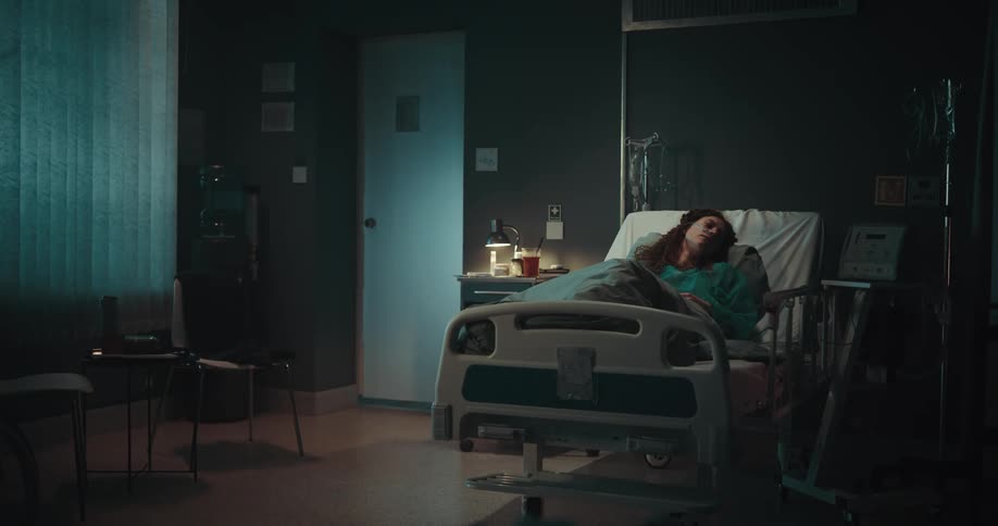 Woman sleeping in a hospital bed at an empty hospital room at night