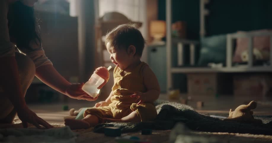 Mother helps toddler drink water from bottle