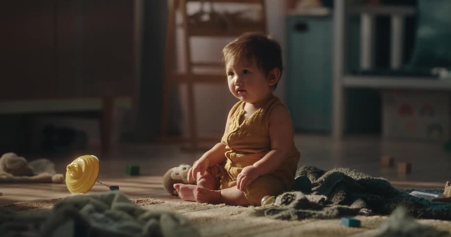 An infant girl playing with toys while sitting on the floor indoor in the morning