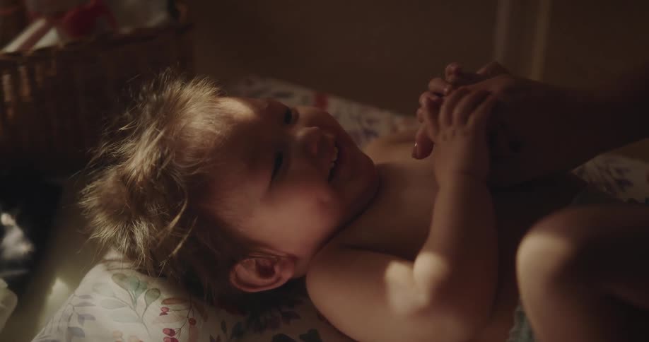 Hand of a person playing with a lying baby who is smiling