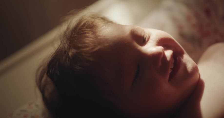 Toddler baby lays downs as person makes them laugh by tickling and kissing