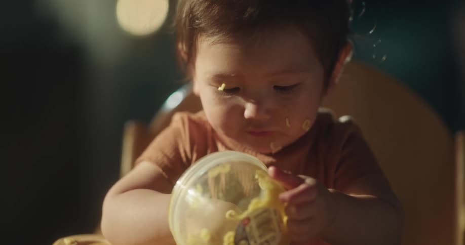 A baby girl is eating pasta with her hands and is smearing it on her face