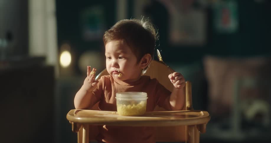 A baby sitting in a high chair messily eats food by hand