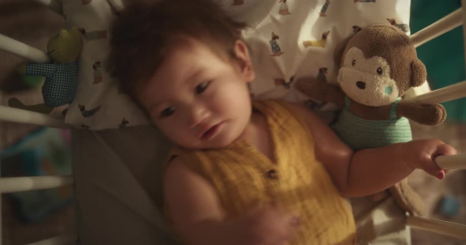 A baby in a crib is crying and then starts to smile
