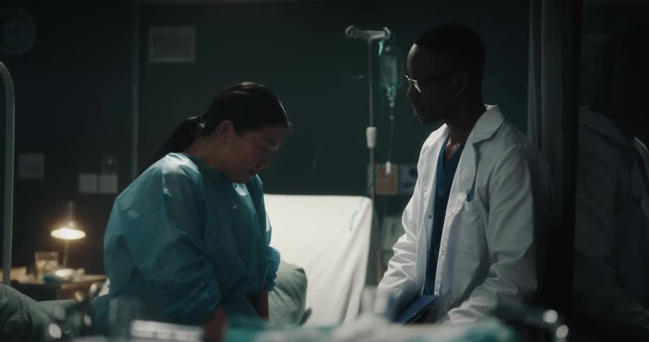 Doctor talking to a patient sitting on the hospital bed looking downcast