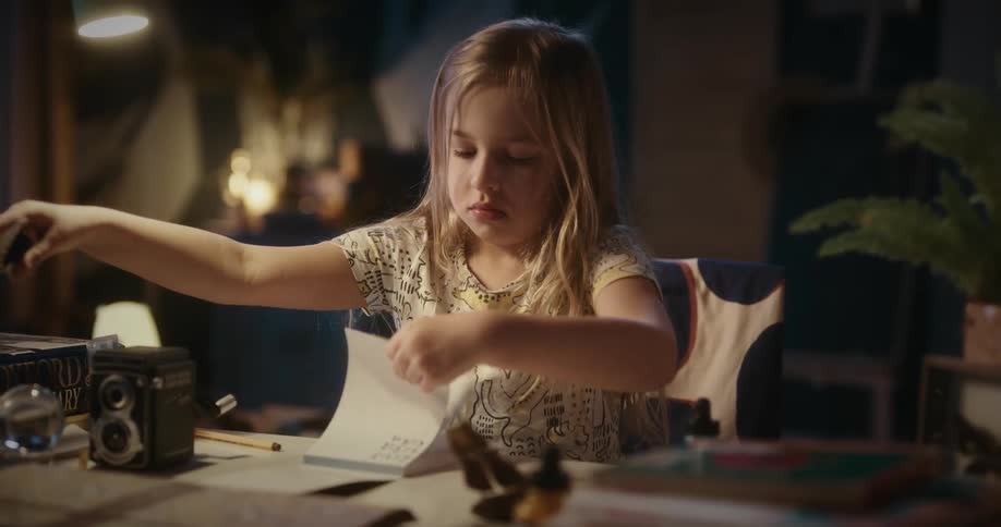 Young girl writing at a table in a warmly lit cozy indoor setting