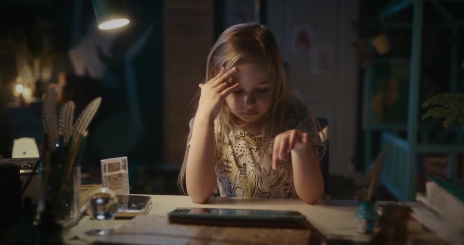 Girl sitting at a desk uses a tablet at night