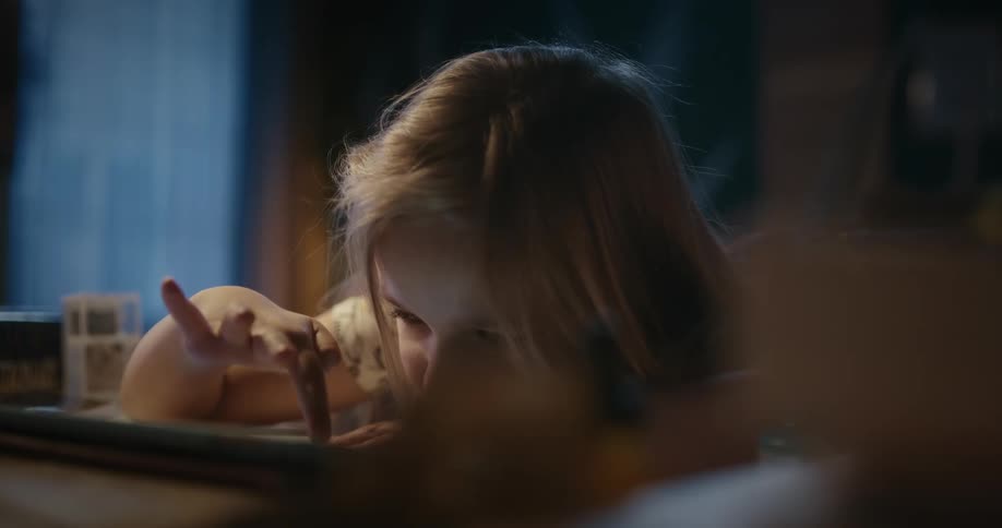 A little girl is sitting at a desk playing with a tablet computer
