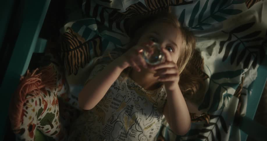 Little girl laying in bed on her back looking up at the glass ball that she is holding in her hands