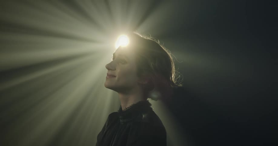 A woman is facing left and tilting her head back against a projector light