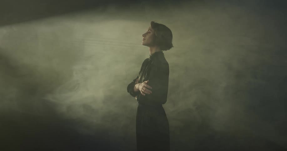 Lady stands alone in a dark room with both arms on her stomach