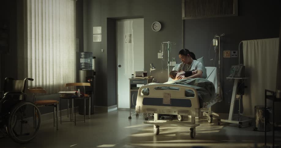 Lady breastfeeds her baby while seated on the hospital bed