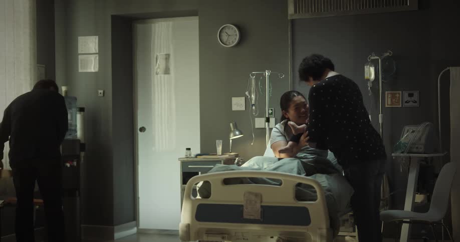 A couple brings a baby to a woman in a hospital bed