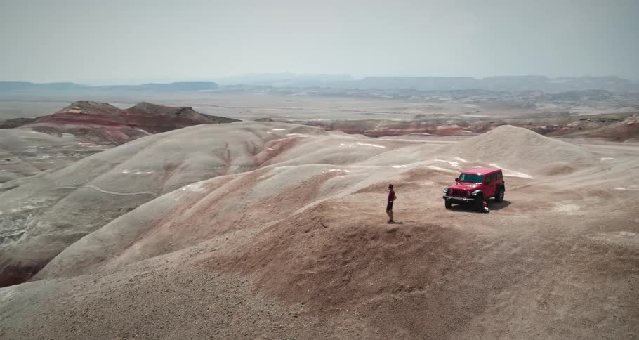 Aerial panorama of a person and a car on the peak of a desert mountain