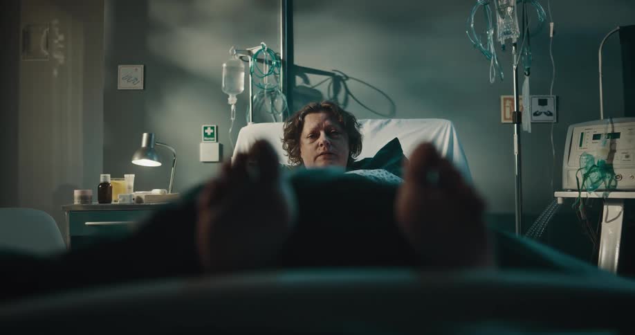 A woman is lying in a hospital bed and talk to a doctor and make faces of sadness