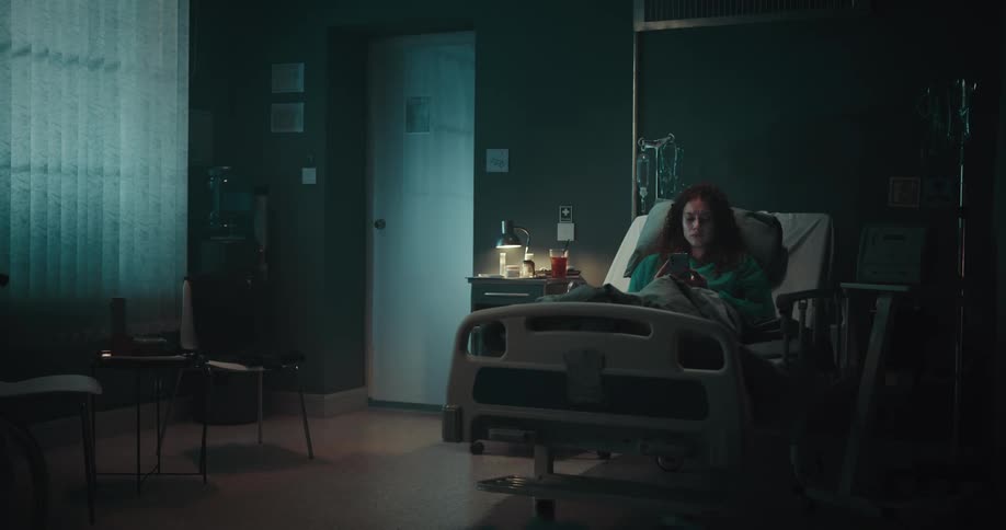 A clip of a female patient laying on a sickbed in the hospital while operating her smart phone