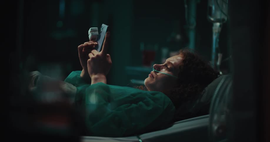 Female operating a mobile phone while laying on the hospital bed with nasogastric tube in her nose at night