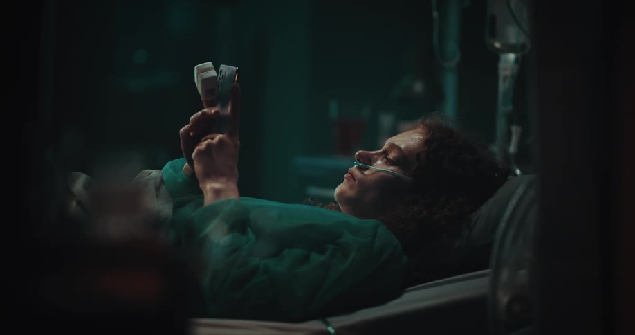 Woman lying in the hospital bed with a nasal cannula using the phone