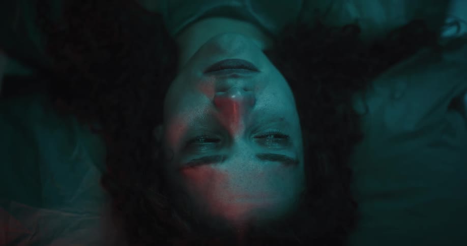 A woman lying in the dark room with a sad look
