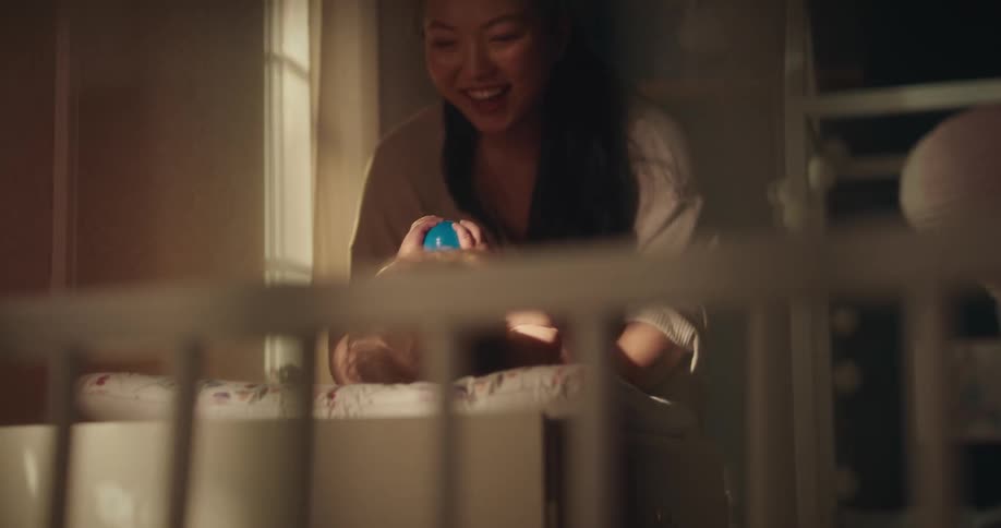 Mother playing with her baby daughter and putting her in a crib