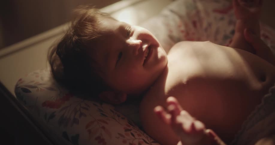 A baby lying in bed and laughing as the mother changes their diaper