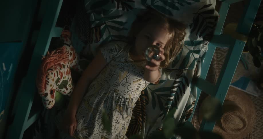 Girl examines glass sphere while lying on bed