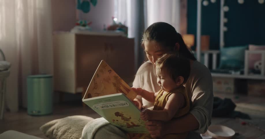 A mother holding a toddler reads a book in a room