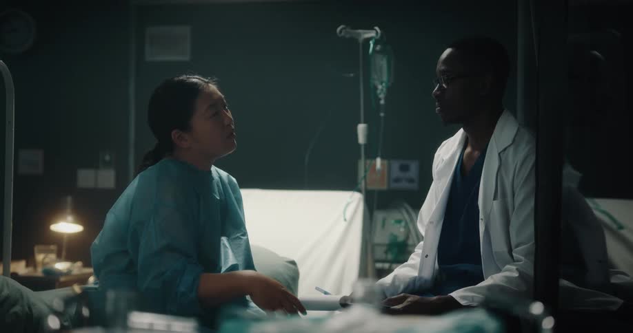 A doctor and a nurse are talking and laughing in front of a hospital bed