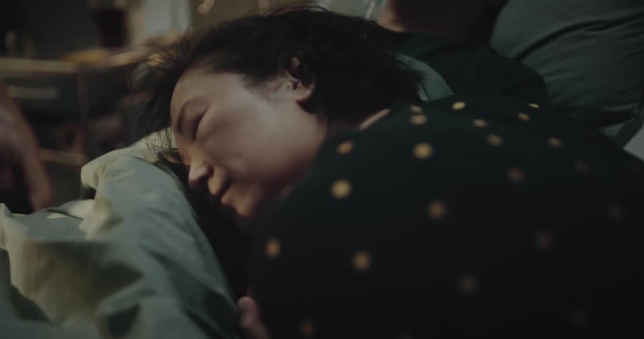 Wife caressing her husband who is lying with an oxygen mask in the hospital and then she lies down with her head on his body