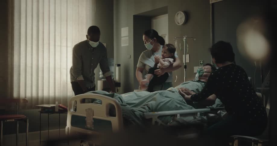 Family arriving and sitting next to a patient who is sleeping in a bed in a hospital room