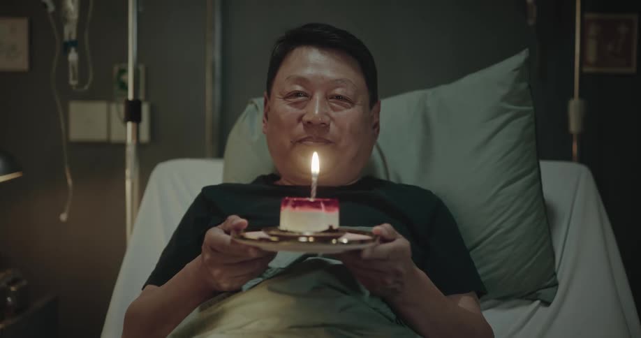 Man in a hospital bed holding a cake and blowing out the candle