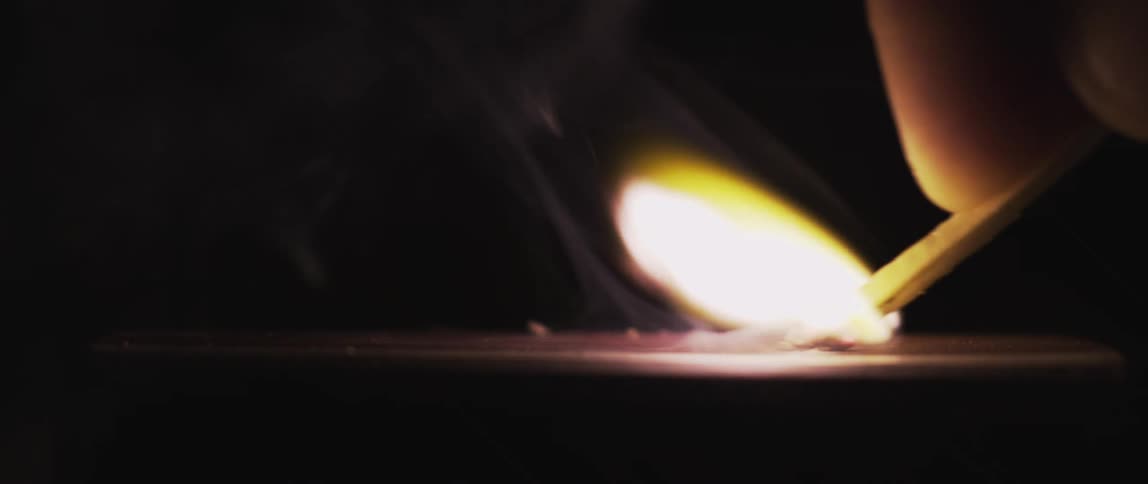 A flame emerges and glows in the darkness as a match is dragged across a surface