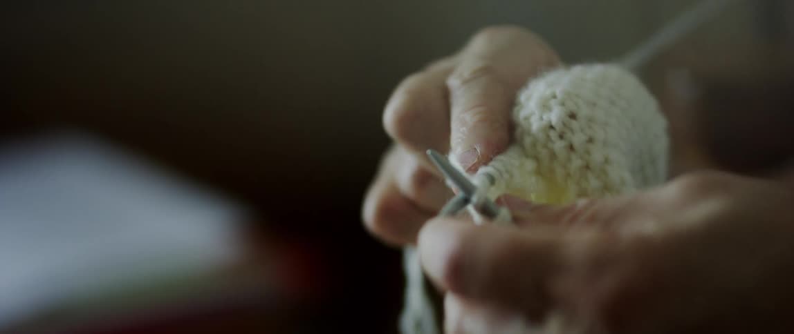 A woman wraps the yarn around the knitting needles as she knits