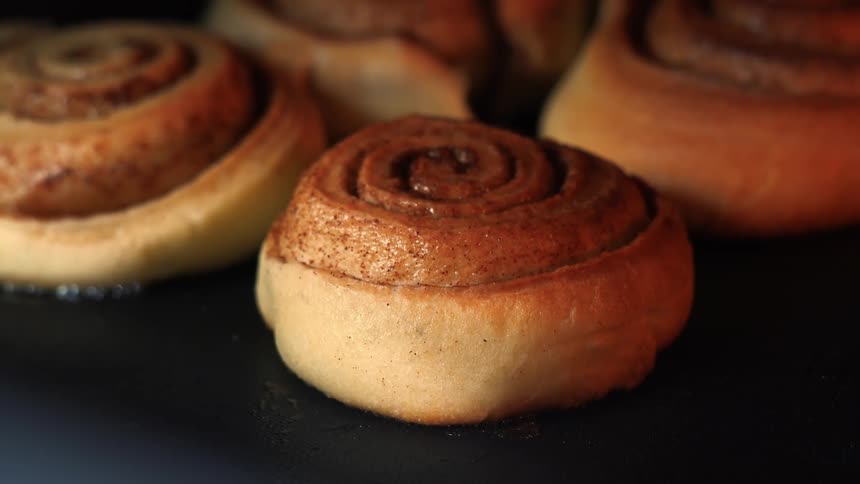 A closeup of cinnamon rolls arranged on a tray baking in the oven