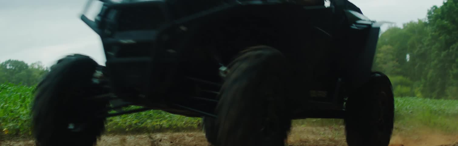 All terrain vehicle drives on dirt road near grove of trees
