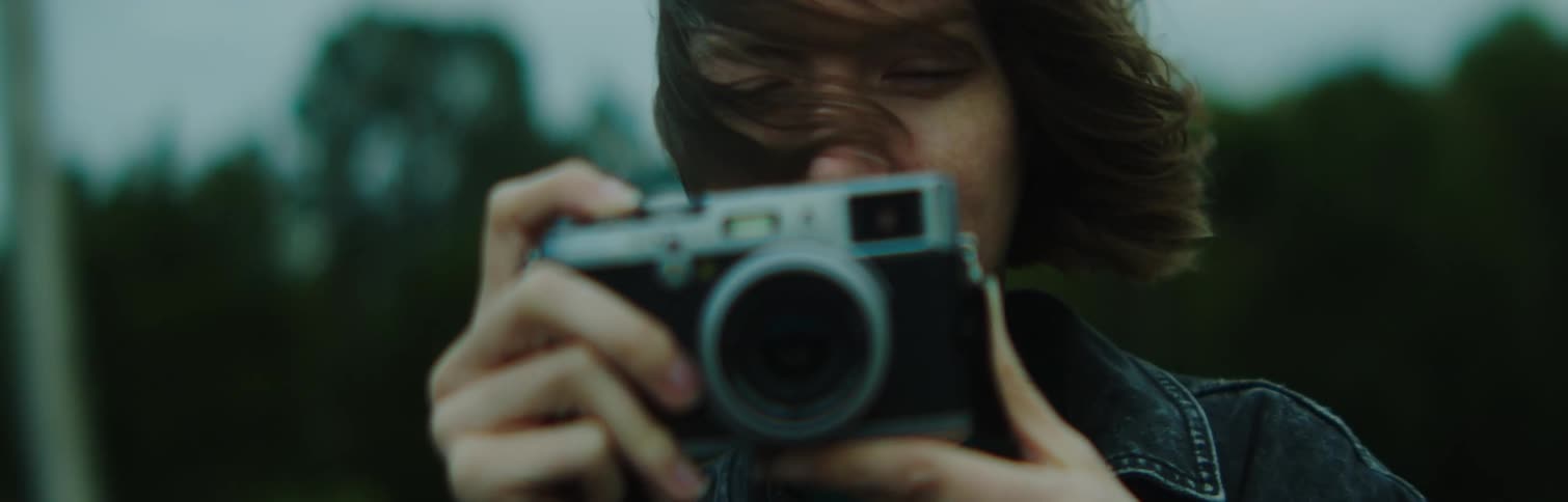 Woman holds camera at nose level wind in her hair outdoors