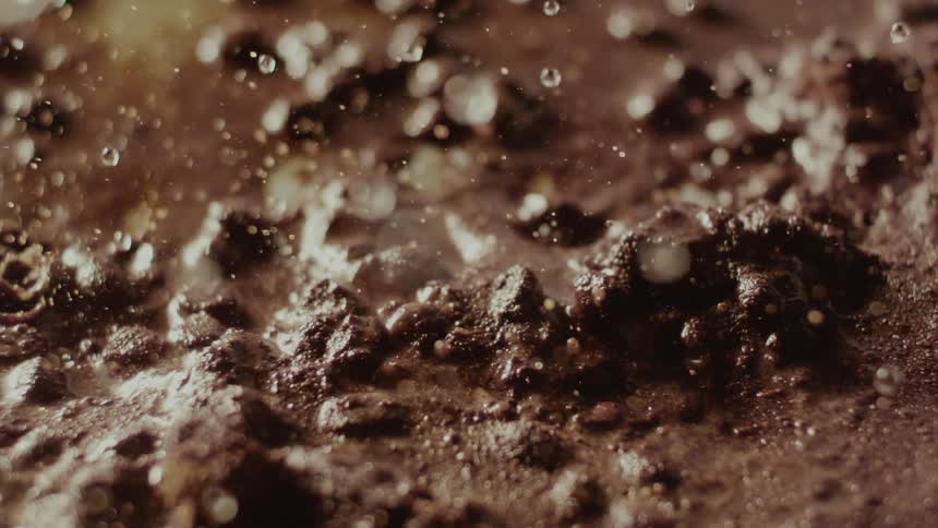 Small water droplets falling onto brown soil in slow motion