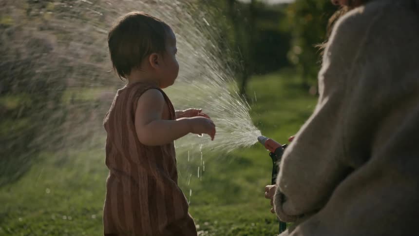 Mother using a hose to spray water on her young daughter