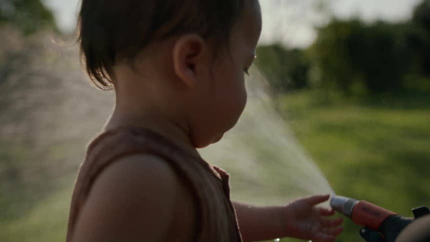 Mother holding a hose with water and her daughter all wet playing