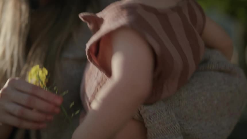 Mother hold a flower to the face of her baby daughter in her arm
