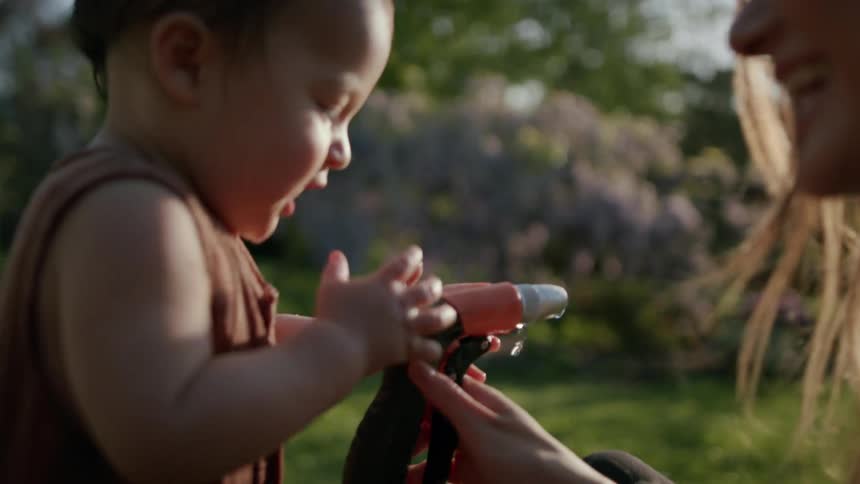 Mother playing with her daughter with a water hose in a garden