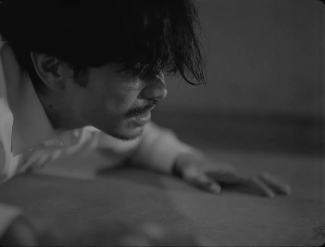 A man is waking up from the ground and he is shirtless and the whole environment is black and white