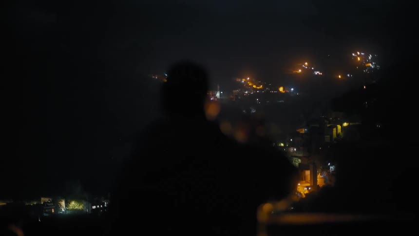 Silhouette of a person facing away overlooking the city from above at night