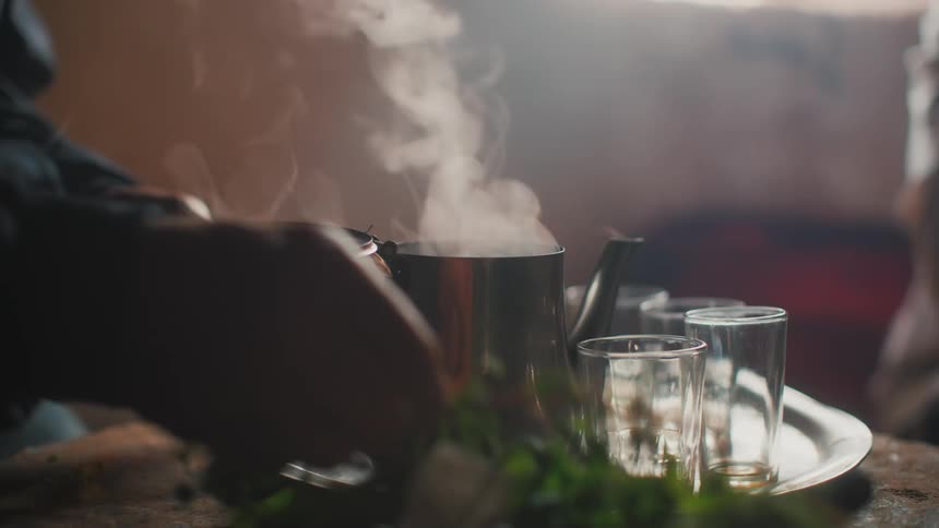 Hands of a person preparing herbs with a kettle of boiling water beside them