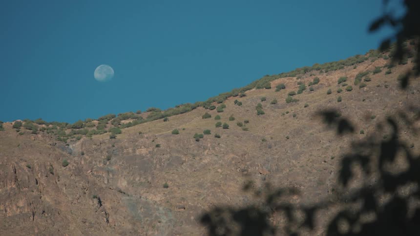 View of a mountain against a clear blue sky with a visible moon during the day